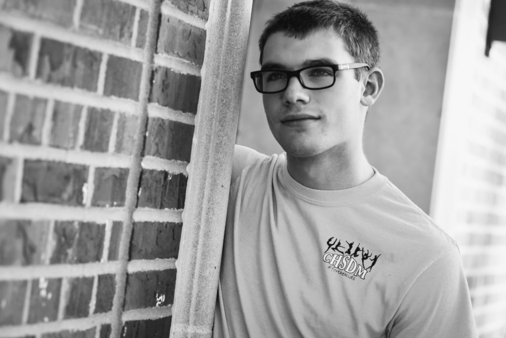 A man with glasses leaning against a brick wall.